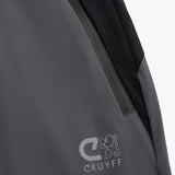 Close-up of a dark gray and black outdoor jacket showing a zippered pocket, a black shoulder panel, and the gray CRUYFF logo on the lower front.