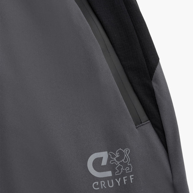 Close-up of a dark gray and black outdoor jacket showing a zippered pocket, a black shoulder panel, and the gray CRUYFF logo on the lower front.
