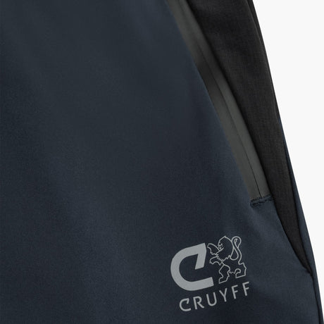 Close-up of a dark navy blue jacket or outerwear piece with a visible gray zipper and a white Cruyff logo printed near the lower left area.