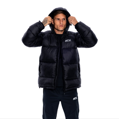 A man wearing a black puffer jacket with a white ATX logo on the chest, posing with the hood up against a solid white background.