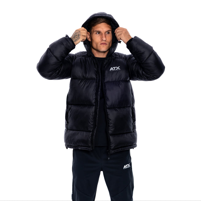 A man wearing a black puffer jacket with a white ATX logo on the chest, posing with the hood up against a solid white background.