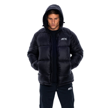 A man wearing a black puffer jacket with a white ATX logo on the chest, paired with matching black pants, shot against a solid white background.