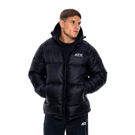 A man wearing a black puffer jacket with a white ATX logo on the chest, paired with black sweatpants, photographed against a solid white background.