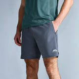 A man wearing dark gray athletic shorts with a white logo on the lower left leg, paired with a green t-shirt and gray running shoes, standing against a light gray studio background.
